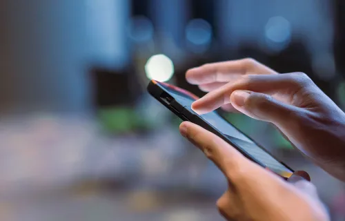 Närbild av en hand som använder en smartphone med pekskärm. Fingret trycker på skärmen i en…