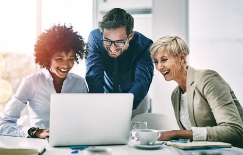 Kuvassa iloisia ihmisiä katsomassa kannettavaa tietokonetta