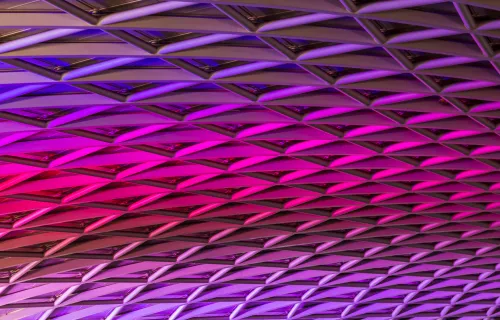 Violetin ja pinkin sävyissä valaistu geometrinen kattokuvio.