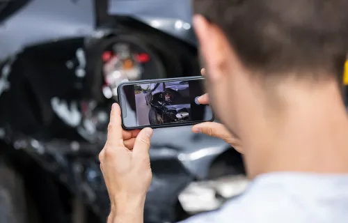 Fahrer dokumentiert einen Fahrzeugschaden mit dem Smartphone für die digitale Schadenaufnahme