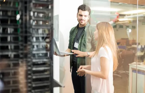 Man and woman conversing in server room with open laptop