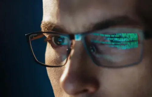 Junger Mann mit Brille, in der sich der Code vom Bildschirm spiegelt