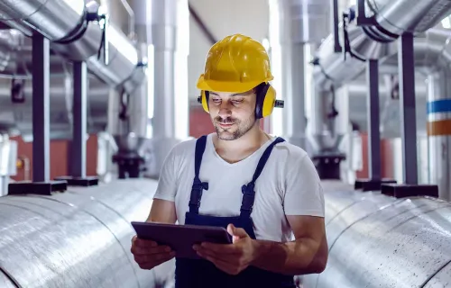 Male worker wearing hardhat looking at a tablet in manufacturing plant