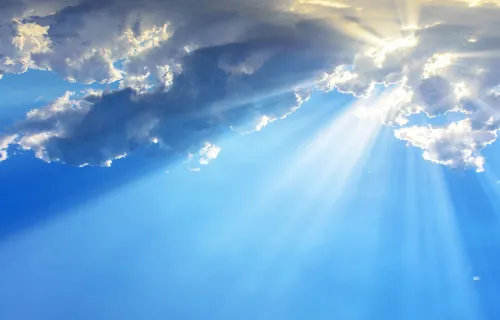 Solstrålar bryter igenom moln på en blå himmel och skapar tydliga ljusstrålar som sprider sig…