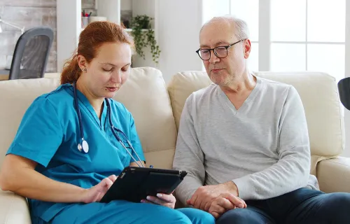 Patient âgé en visioconférence avec un médecin depuis son domicile à l’aide d’un ordinateur…