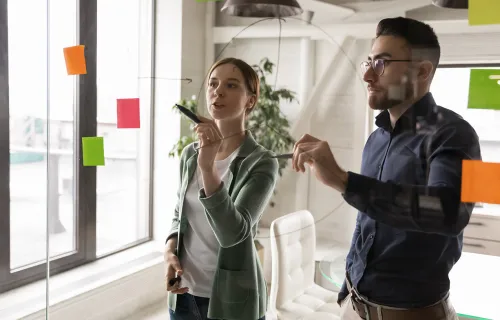 Zwei Berater stehten vor einer Glaswand mit Postit