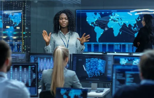 a woman speaking to colleagues in a control room