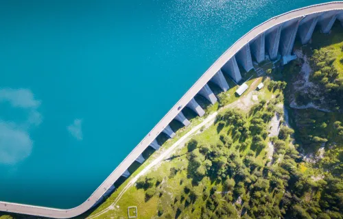 Un barrage hydroélectrique vu du ciel, entouré de reliefs verdoyants, retenant une étendue d…