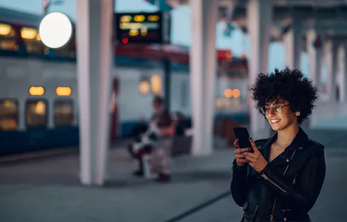 Eine Frau am Bahnhof nutzt ihr Smartphone für die digitale Servicekommunikation