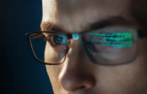 Nærbilde av mann med briller, grønn datakode reflektert i glassene.