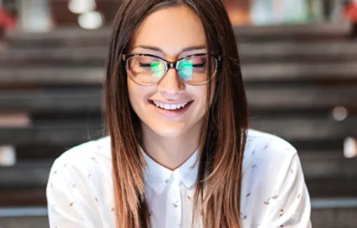 Lähikuva hymyilevästä asiantuntijasta, jolla on silmälasit ja ruskeat hiukset ja joka käyttää tablettia istuessaan portailla