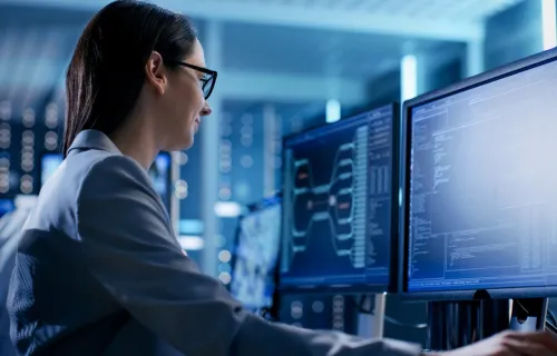 Softwareentwicklerin arbeitet an zwei Bildschirmen mit geöffnetem Programmcode.