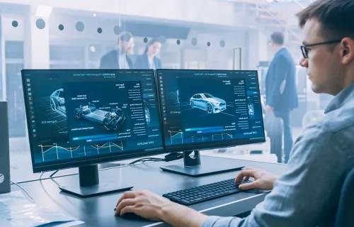 Male data scientist looking at two computer screens car factory