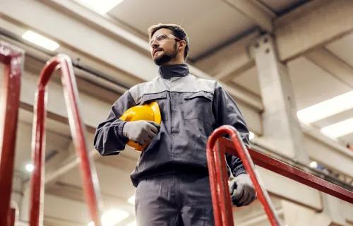 Male industrial factory worker with safety glasses holding hard hat