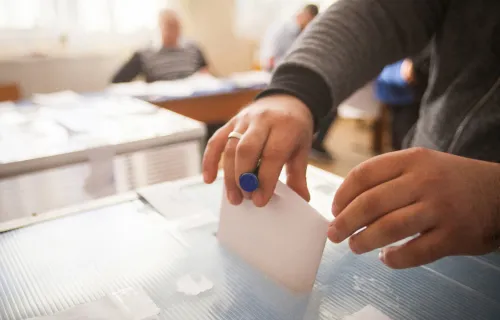 Man steht in einem Wahllokal und gibt seinen Stimmzettel ab