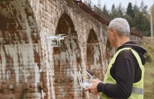 Man in high vis vest flying CGI machine vision drone near bridge