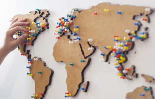 Eine Weltkarte ist mit Stecknadeln besetzt und eine Person steckt gerade eine weitere dazu