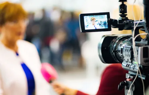 Eine Frau steht verschwommen vor einer Kamera und beantwortet Interviewfragen