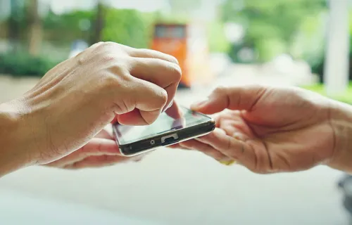 En hand som håller fram en mobiltelefon där en annan persons hand rör skärmen