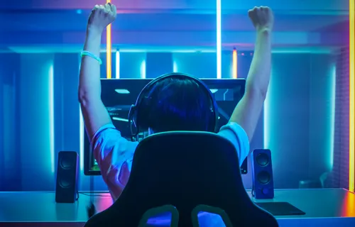 En person höjer armarna i segergest över huvudet vid framgång i e-sport matchen på sin skärm