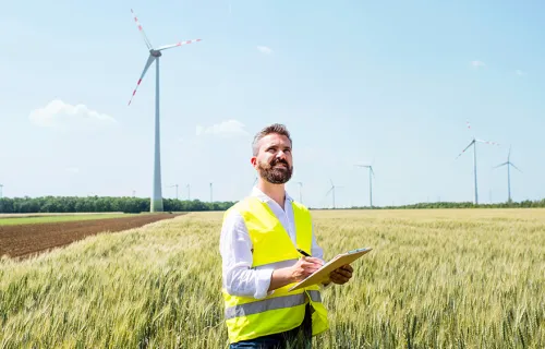 energy and utilities worker in field with wind turbine