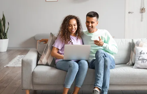 Hymyilevä pariskunta istuu sohvalla ja katselee tietokonetta