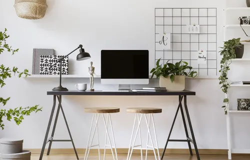 Desk with laptop screen, plants, two stools and lamp