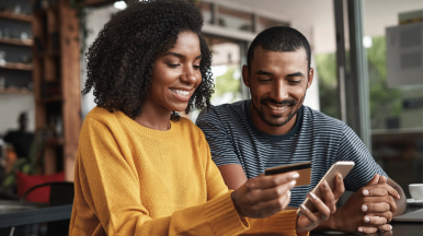 Two people smiling whilst looking at a phone and payment card