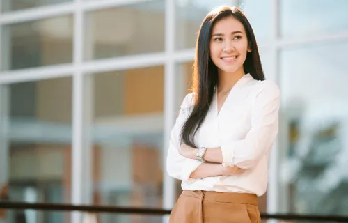 woman in officewear smiles outside with folded arms