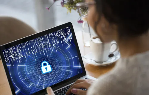 Kvinna ses bakifrån där hon tittar på sin surfplatta som har ett stort hänglås på den blåa skärmen som symboliserar cybersecurity