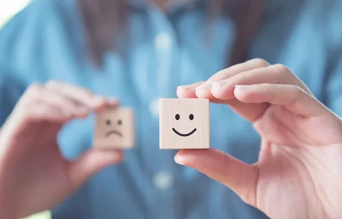 Person holding two wooden dice, one with a smiley face and one with a sad face showing sentiment