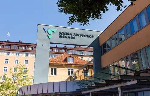 Entrén till Södra Älvsborgs sjukhus med ett gult bostadshus i bakgrunden och blå sommarhimmel