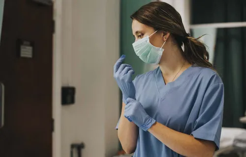 Female healthcare professional wearing a mask and pulling on gloves