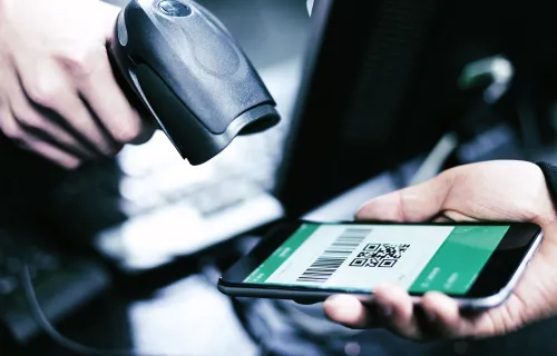 En person håller en smartphone med en QR-kod medan en annan skannar koden med en handscanner…