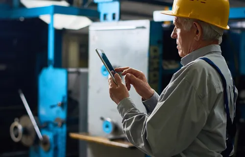 En eldre mann sjekker mobilen på fabrikken