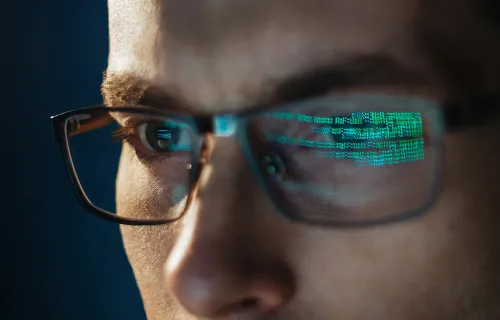 Nærbilde av mann med briller, grønn datakode reflektert i glassene.