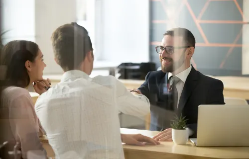 A couple and a consultant shaking hands across a desk