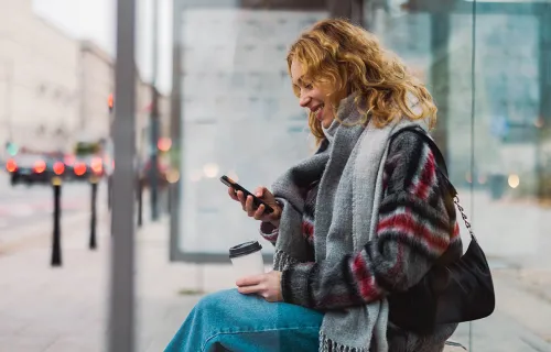 young woman waiting for public transport and looking at her phone