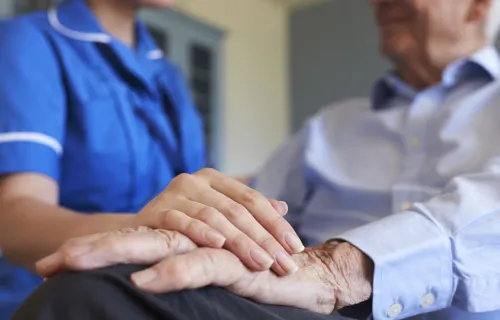 Pflegerin hat ihre Hand auf die eines älteren Patienten gelegt