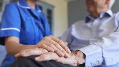 Pflegerin hat ihre Hand auf die eines älteren Patienten gelegt