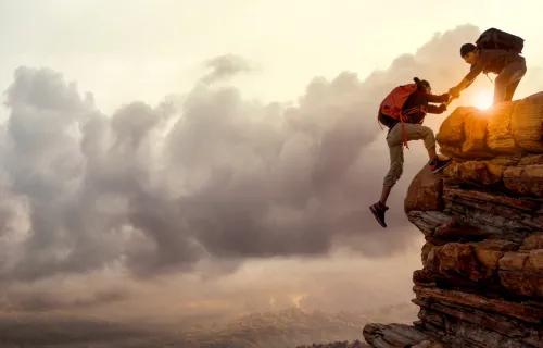 Zwei Menschen unterstützen sich gegenseitig beim Bergaufstieg bei Sonnenaufgang.