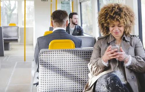 Ung kvinna sitter och chattar via sin mobiltelefon på buss
