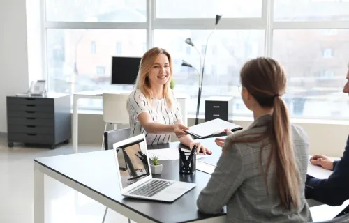 A person handing a document to another person across a desk