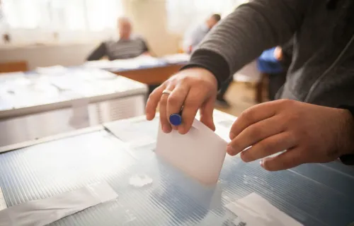 Eine Person wirft einen Wahlschein in eine Wahlurne