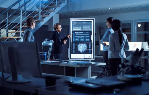 Project team standing meeting around a large digital display