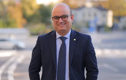 Porträtt av en leende man i kostym och slips, stående utomhus i en stadsmiljö med suddig…