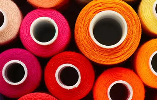 Färgladda rullar med sytråd som ligger staplade på varandra sorterat per färg