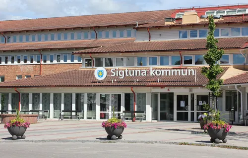 Entrén till Sigtuna kommuns kommunhus med skylten "Sigtuna kommun" ovanför ingången. Byggnaden…