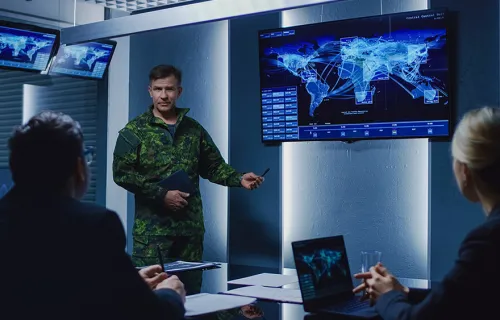Man i militärkläder står vid en skärm som visar en världskarta framför en grupp människor