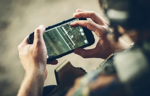 Närbild av en person i militäruniform som håller en smartphone med en digital karta eller…